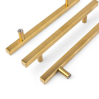 Trois poignées Marano Gold de yessential.fr, présentant un design rectangulaire moderne avec deux points de montage, sont placées en diagonale sur un fond blanc - parfaites comme accents minimalistes pour des armoires ou des tiroirs contemporains.