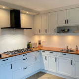 Cuisine moderne avec Leonardo Black Deluxe de yessential.fr : placards blancs, plan de travail en bois, poignées luxe, cuisinière à gaz avec hotte aspirante noire, évier, éclairage sous meuble, ainsi que des bouteilles, des couteaux et une bouteille de vin sur le plan de travail et l'étagère.