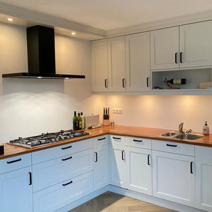 Cuisine moderne avec Leonardo Black Deluxe de yessential.fr : placards blancs, plan de travail en bois, poignées luxe, cuisinière à gaz avec hotte aspirante noire, évier, éclairage sous meuble, ainsi que des bouteilles, des couteaux et une bouteille de vin sur le plan de travail et l'étagère.