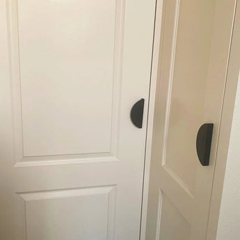 Deux portes Torno Black de yessential.fr, installées côte à côte, ont des poignées en forme de croissant qui se chevauchent. En raison de leur proximité, les deux portes ne peuvent pas être complètement ouvertes en même temps.