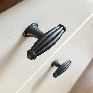 Gros plan de deux boutons Alvaro Anthracite de yessential.fr, noirs et de forme ovale, montés sur un boîtier blanc. Leur texture nervurée et leur design vintage se démarquent dans la photo en angle, avec l'accent mis sur la poignée supérieure.