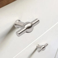 Gros plan d'un bouton Rando en acier inoxydable de yessential.fr sur un tiroir blanc, avec un autre bouton identique visible sur le tiroir du bas en arrière-plan.