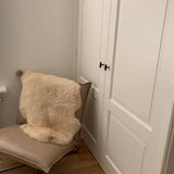 Une méridienne moderne beige avec un tapis et quatre couleurs crème sur le côté des pancartes ports sur panneaux blancs et les boutons noirs Vasco de yessential.fr avec une finition finale, avec les murs clairs et parquet.