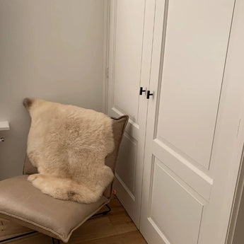 Une méridienne moderne beige avec un tapis et quatre couleurs crème sur le côté des pancartes ports sur panneaux blancs et les boutons noirs Vasco de yessential.fr avec une finition finale, avec les murs clairs et parquet.
