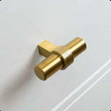 Un gros plan du bouton Arturo Gold de yessential.fr, avec un design en forme de T en or mat monté sur un tiroir à panneaux blancs - un choix idéal pour un intérieur champêtre.