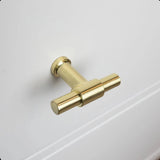 Idéal pour les boutons d'armoires de cuisine, le bouton 10x Cordero Gold de yessential.fr est présenté installé sur une porte d'armoire blanche avec des détails de panneau subtils.