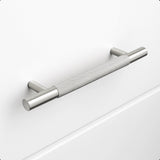 Le Remo Stainless Steel Deluxe de yessential.fr est une poignée d'armoire en acier inoxydable brossé avec une texture de poignée, montée horizontalement sur un tiroir blanc uni. Il possède des supports cylindriques et offre un design moderne et minimaliste.