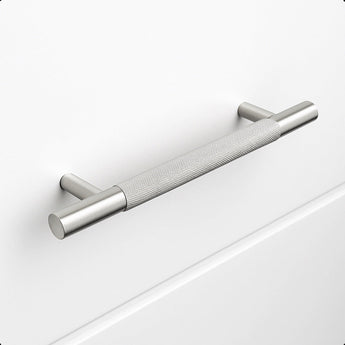 Le Remo Stainless Steel Deluxe de yessential.fr est une poignée d'armoire en acier inoxydable brossé avec une texture de poignée, montée horizontalement sur un tiroir blanc uni. Il possède des supports cylindriques et offre un design moderne et minimaliste.
