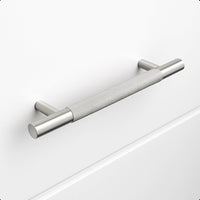 Le Remo Stainless Steel Deluxe de yessential.fr est une poignée d'armoire en acier inoxydable brossé avec une texture de poignée, montée horizontalement sur un tiroir blanc uni. Il possède des supports cylindriques et offre un design moderne et minimaliste.
