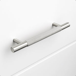 Le Remo Stainless Steel Deluxe de yessential.fr est une poignée d'armoire en acier inoxydable brossé avec une texture de poignée, montée horizontalement sur un tiroir blanc uni. Il possède des supports cylindriques et offre un design moderne et minimaliste.