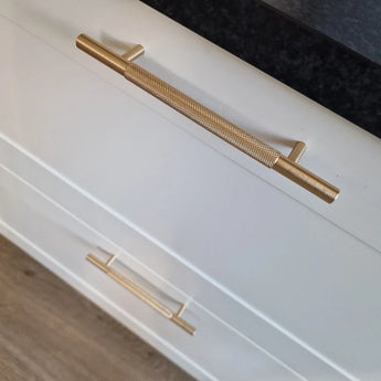 Gros plan de deux tiroirs Remo Gold Deluxe de yessential.fr, avec d'élégantes poignées dorées, sur un comptoir sombre et un parquet clair.