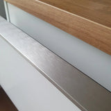 Gros plan d'un meuble de cuisine Enzo en acier inoxydable yessential.fr, avec une poignée profilée de couleur acier inoxydable, une façade blanche et un plan de travail en bois pour un look épuré et minimaliste.