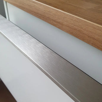 Gros plan d'un meuble de cuisine Enzo en acier inoxydable yessential.fr, avec une poignée profilée de couleur acier inoxydable, une façade blanche et un plan de travail en bois pour un look épuré et minimaliste.
