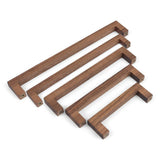 Quatre poignées en noyer Vasco de yessential.fr en bois de noyer, disposées en diagonale du grand au petit sur fond blanc. Chaque poignée comporte des trous de vis visibles aux deux extrémités.