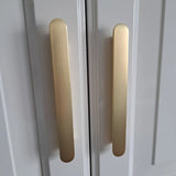 Gros plan de deux poignées verticales Arriero Gold Deluxe de yessential.fr, montées sur des portes d'armoires blanches au design moderne et minimaliste.