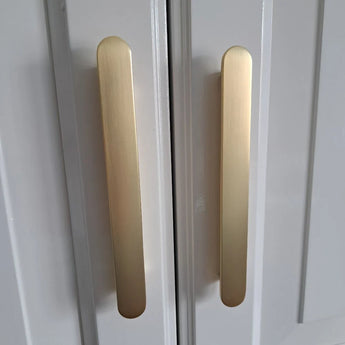 Gros plan de deux poignées verticales Arriero Gold Deluxe de yessential.fr, montées sur des portes d'armoires blanches au design moderne et minimaliste.