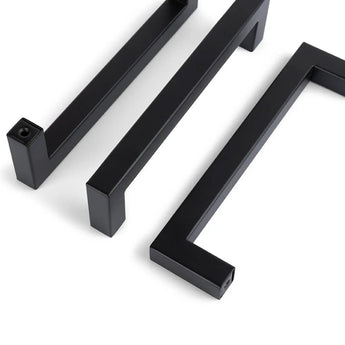 Trois poignées d'armoire Vasco Black de yessential.fr sont placées en diagonale sur un fond blanc. Chaque poignée présente un design moderne et minimaliste avec des lignes épurées et des angles vifs.