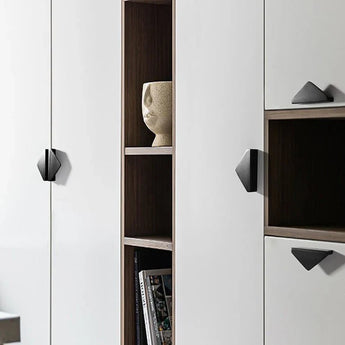 Gros plan d'une armoire blanche moderne avec des poignées Triano Black 64 mm de yessential.fr, avec des étagères en bois ouvertes contenant un vase rond texturé et quelques livres.