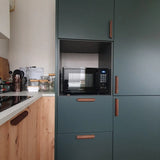 Une cuisine moderne avec des poignées en noyer Lucasso de yessential.fr, des armoires vertes, un micro-ondes intégré et un comptoir en bois avec casseroles et ustensiles - une touche parfaite pour un décor naturel.