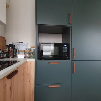 Une cuisine moderne avec des poignées en noyer Lucasso de yessential.fr, des armoires vertes, un micro-ondes intégré et un comptoir en bois avec casseroles et ustensiles - une touche parfaite pour un décor naturel.
