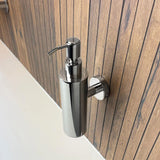 Le distributeur de savon Alberto Chrome de yessential.fr est élégant et est fixé au mur sur un mur vertical en bois au-dessus d'un comptoir blanc.