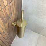 L'ensemble de toilettes Lorenzo Gold de yessential.fr est élégamment monté sur les panneaux muraux en bois à côté du carrelage gris clair dans le coin de la salle de bain. Parfait comme accessoire de toilette de luxe ou dans le cadre d'un ensemble d'accessoires.