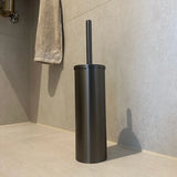L'ensemble WC Juano Gunmetal (sans perçage) de yessential.fr repose sur des carreaux clairs avec une serviette beige à proximité - un ajout élégant à votre collection d'accessoires de salle de bain ou d'accessoires de toilettes.