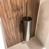 L'ensemble WC Lauro Gunmetal de yessential.fr est un porte-brosse de toilette en métal élégant avec une poignée verticale, monté sur un mur lambrissé en bois à côté de carreaux de couleur claire, parfait pour les collections d'accessoires de salle de bain de luxe.
