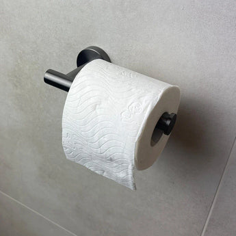 Un rouleau de papier toilette avec un motif en relief ondulé est suspendu au porte-rouleau de papier toilette Tino Gunmetal de yessential.fr, monté sur un mur carrelé gris clair pour un ajout élégant et moderne à vos accessoires de salle de bain.