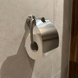 Un rouleau de papier toilette est fixé au mur sous le support brillant en acier inoxydable Julio de yessential.fr, un support en métal élégant qui se fixe aux murs carrelés de couleur claire de la salle de bain.