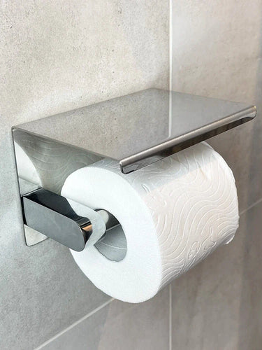 Un rouleau de papier toilette est monté sur le Tazio Chrome de yessential.fr, un élégant support chromé avec un dessus plat, fixé à un mur carrelé gris.