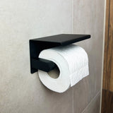 Un rouleau de papier toilette est monté sur l'ensemble WC Donato Black de yessential.fr, fixé sur le mur de la salle de bain bain carrelé beige avec un panneau devant.