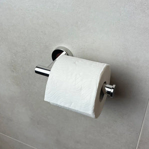 Un rouleau de papier toilette blanc repose sur le porte-rouleau de papier toilette Tino Chrome de yessential.fr, monté contre un mur carrelé gris clair - un ajout élégant à vos accessoires de salle de bain.