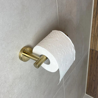 Un rouleau de papier toilette est monté sur le porte-rouleau de papier toilette Tino Gold de yessential.fr, fixé au mur carrelé de la salle de bain - un accessoire subtil mais luxueux qui ajoute un aspect luxueux à n'importe quelle pièce.