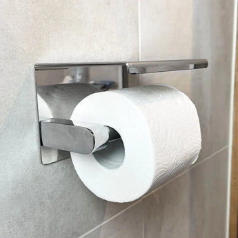 Un rouleau de papier toilette sur l'élégant porte-rouleau de papier toilette Tazio Chrome de yessential.fr, monté sur un mur carrelé de salle de bain. Le support métallique moderne ajoute de l'élégance avec un motif en relief sur le papier.