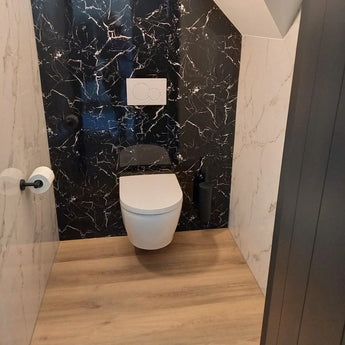 Une salle de bain moderne avec les toilettes murales yessential.fr Tino Black, paroi arrière en marbre noir, murs blancs, parquet en bois, accessoires noir mat et un porte-rouleau papier toilette en acier inoxydable sur le mur de gauche.