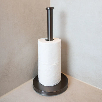 L'ensemble de toilettes Delo Gunmetal (sans perçage) de yessential.fr comprend deux rouleaux de papier toilette et est placé dans une pièce d'angle avec des murs et des surfaces carrelées de couleur claire.