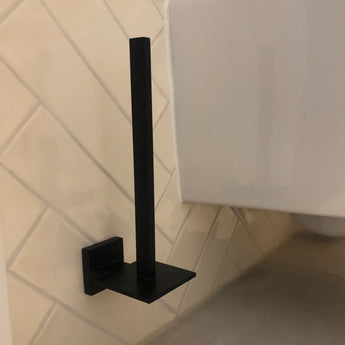 L'ensemble de toilettes Moreno Black de yessential.fr, en noir mat élégant, est monté au mur dans une salle de bain carrelée. Une mise à niveau parfaite et élégante pour vos accessoires de salle de bain ou de toilettes. Toilettes partiellement visibles ; rouleau de papier toilette non inclus.