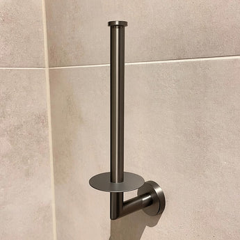 La porte de toilette en papier yessential.fr de Roberto Gunmetal présente un look métallique élégant avec un pot vertical minimaliste et une plaque de base ronde, présentée sur un mur beige.