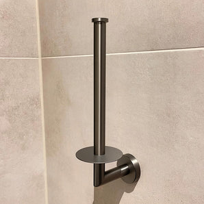 La porte de toilette en papier yessential.fr de Roberto Gunmetal présente un look métallique élégant avec un pot vertical minimaliste et une plaque de base ronde, présentée sur un mur beige.