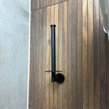 L'ensemble WC Pacho Black de yessential.fr comprend un support WC mural noir, installé verticalement sur un mur avec du carrelage à motif bois à côté du carrelage gris. Le conteneur est vide.