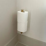 Deux rouleaux de papier toilette sont empilés sur un support mural dans le coin d'une salle de bain aux teintes claires, ajoutant de l'élégance lorsqu'ils sont associés à l'ensemble WC Fabiano Gold de yessential.fr.