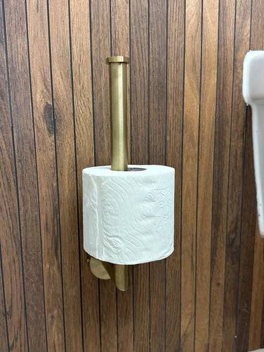 Un rouleau de papier toilette repose sur un support vertical en laiton de l'ensemble WC Corrado Gold de yessential.fr, monté sur un mur en bois à côté d'un lavabo blanc.