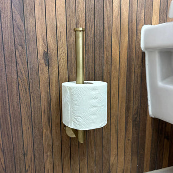 Un seul rouleau de papier toilette est tenu par l'ensemble WC Pacho Gold de yessential.fr, avec un support en laiton monté sur un panneau en bois à proximité d'un lavabo blanc.