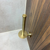 Idéal pour les accessoires de salle de bain, le porte-rouleau de papier toilette Roberto Gold de yessential.fr est monté sur un panneau en bois à côté des murs et du sol carrelés - présenté ici sans papier toilette.