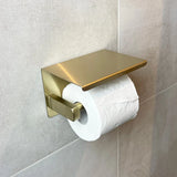 Le porte-rouleau de papier toilette est en or mat et monté sur un mur carrelé gris clair – une touche élégante pour tout ensemble d'accessoires de salle de bain ou de toilette carré.