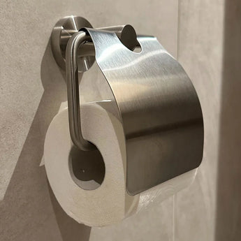 L'ensemble de toilettes Marino en acier inoxydable de yessential.fr comprend un rouleau de papier toilette sur un support mural fin avec un couvercle en métal incurvé brillant - parfait pour ajouter une touche moderne au décor de votre salle de bain.