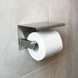 Un rouleau de papier toilette blanc sur un ensemble de toilettes moderne en acier inoxydable Donato de yessential.fr, fixé au mur contre un mur de salle de bains carrelé gris clair.