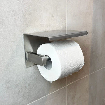 Un rouleau de papier toilette blanc sur un ensemble de toilettes moderne en acier inoxydable Donato de yessential.fr, fixé au mur contre un mur de salle de bains carrelé gris clair.