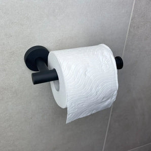 Un rouleau de papier toilette avec une vague en relief et un motif floral est suspendu à un porte-rouleau de papier toilette Tino Black de yessential.fr, fixé à un mur carrelé gris clair.